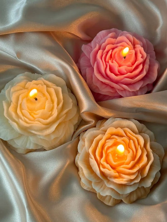 Three flower-shaped candles on a satin surface