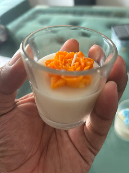 Hand holding Fiorance Luxe floral soy wax candle in a glass cup with orange flower design