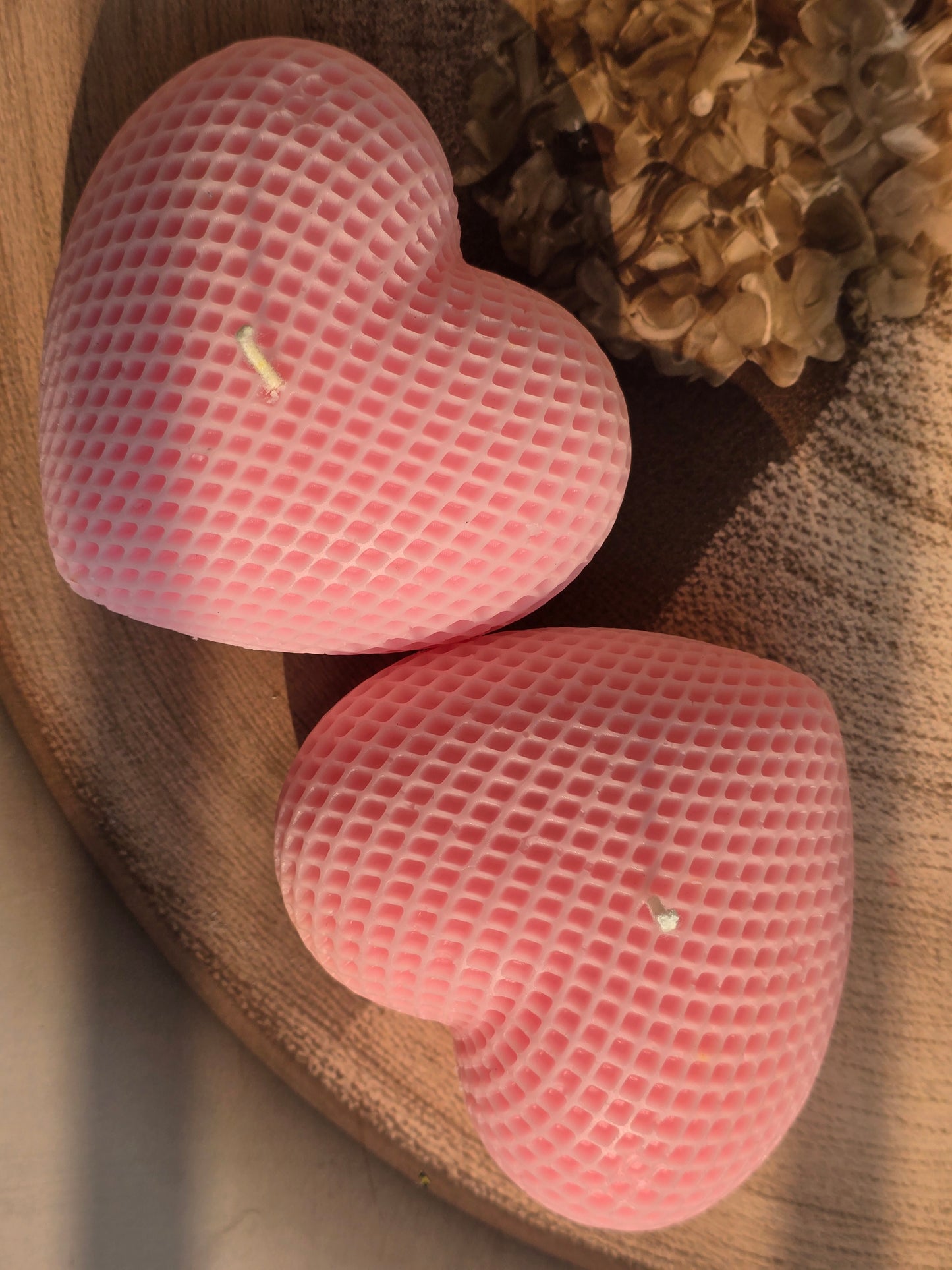 Two pink heart-shaped objects on a wooden surface with a textured background
