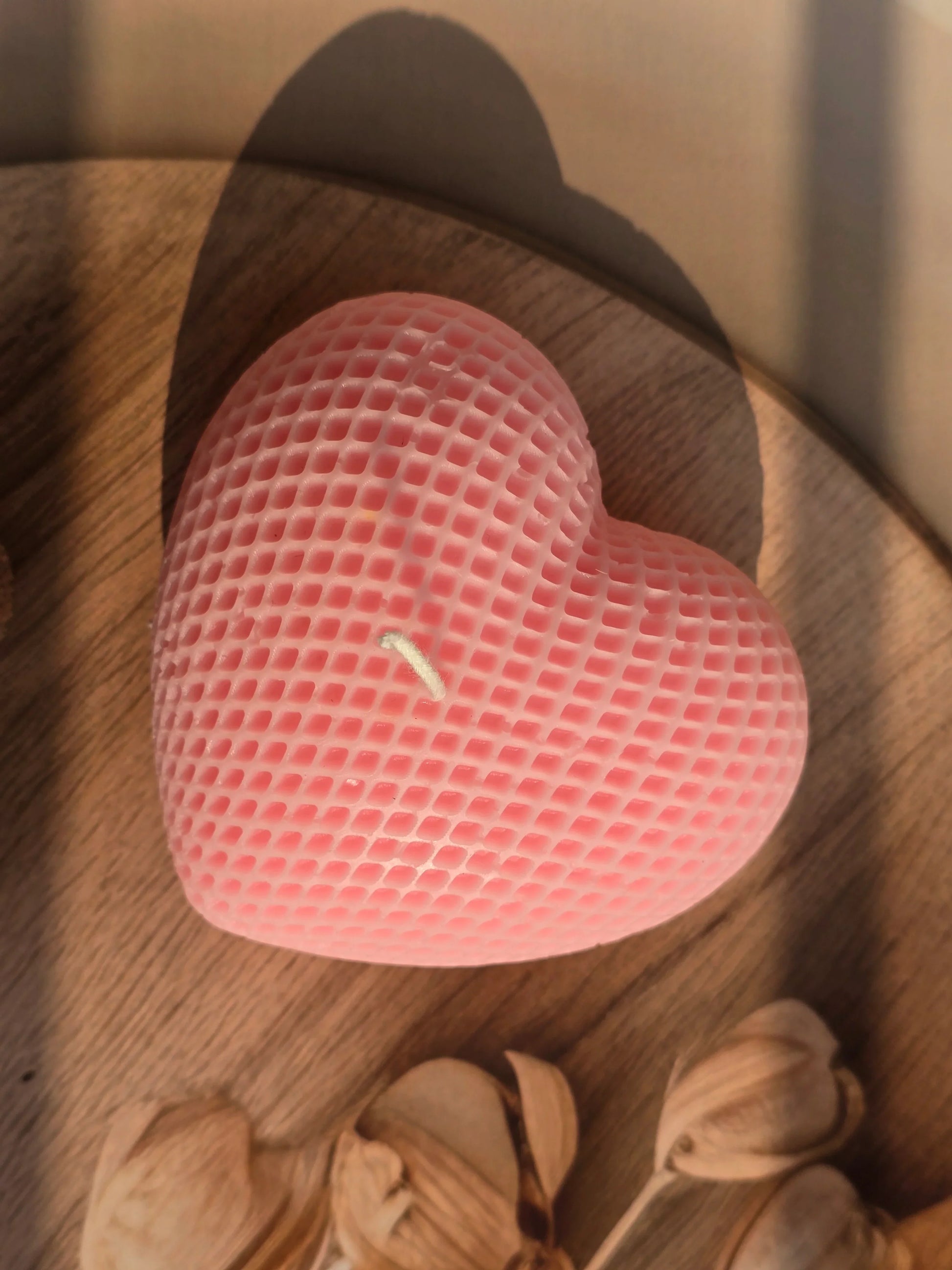 Heart-shaped pink object on a wooden surface with flowers in the background