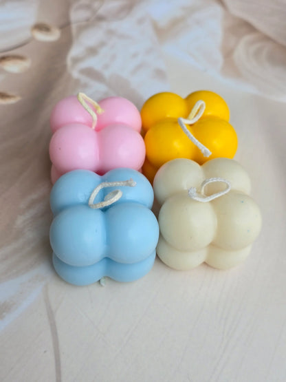 Four pastel Fiorance Luxe soy wax bubble candles in yellow, pink, blue, and cream on beige fabric.