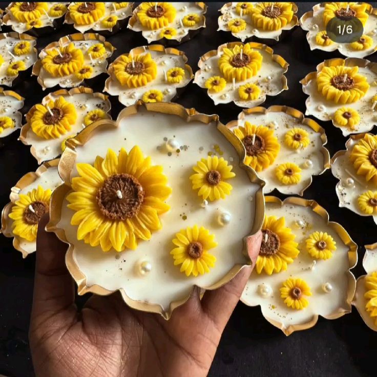 Hand holding a handcrafted soy wax candle with sunflower design by Fiorance Luxe, surrounded by similar floral candles.