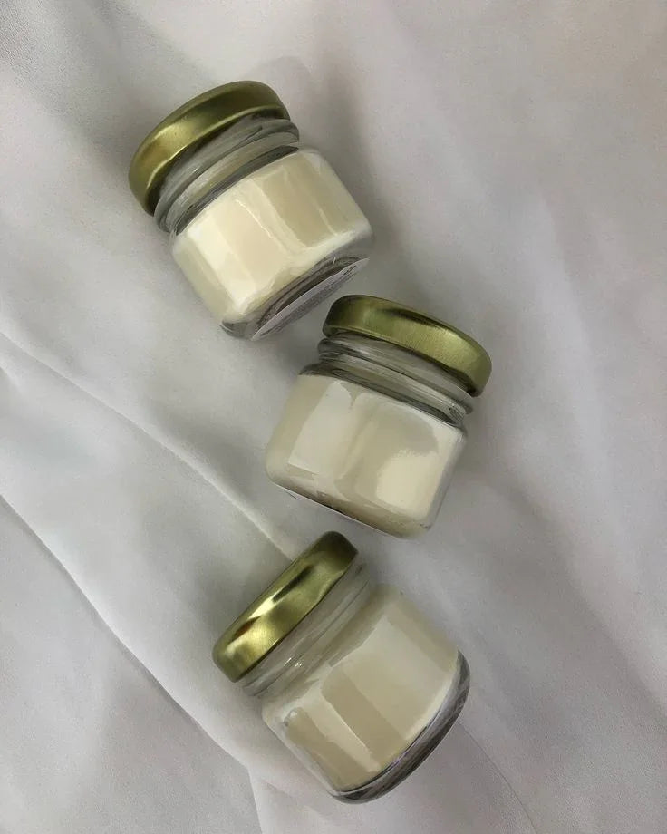 Three Fiorance Luxe soy wax candles in glass jars with gold lids on a white fabric background