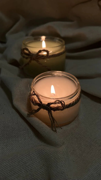 Handcrafted soy wax candles in glass jars with twine bows, lit on a fabric background
