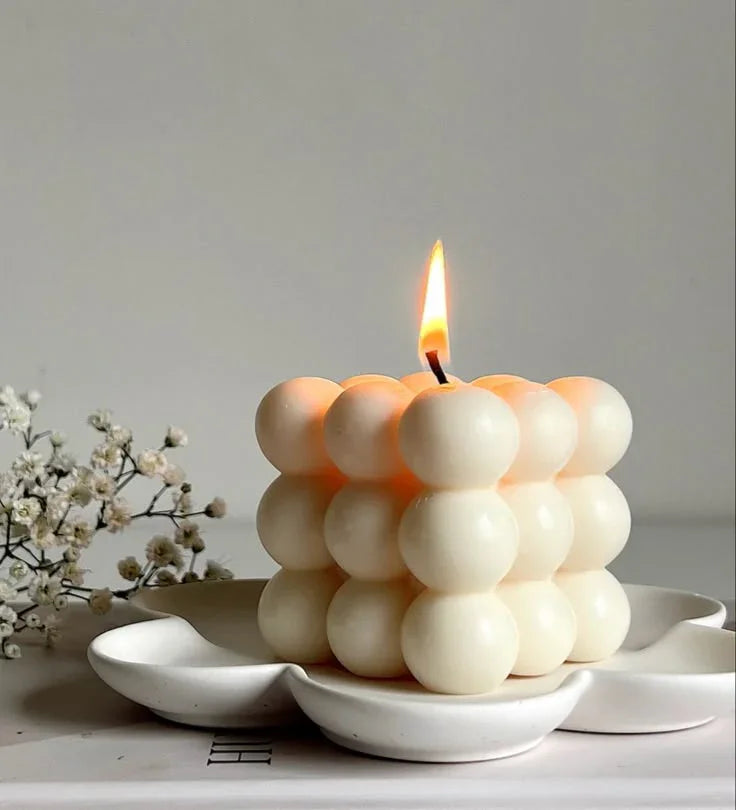 Cube-shaped soy wax bubble candle lit, on a white tray, with small white flowers, Fiorance Luxe