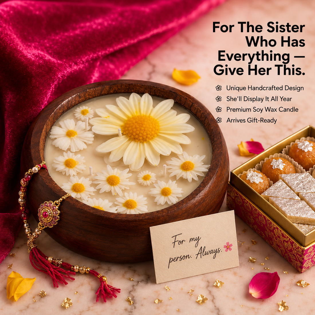 Decorative candle with flowers in a wooden bowl, accompanied by a gift box and card, on a pink fabric background.