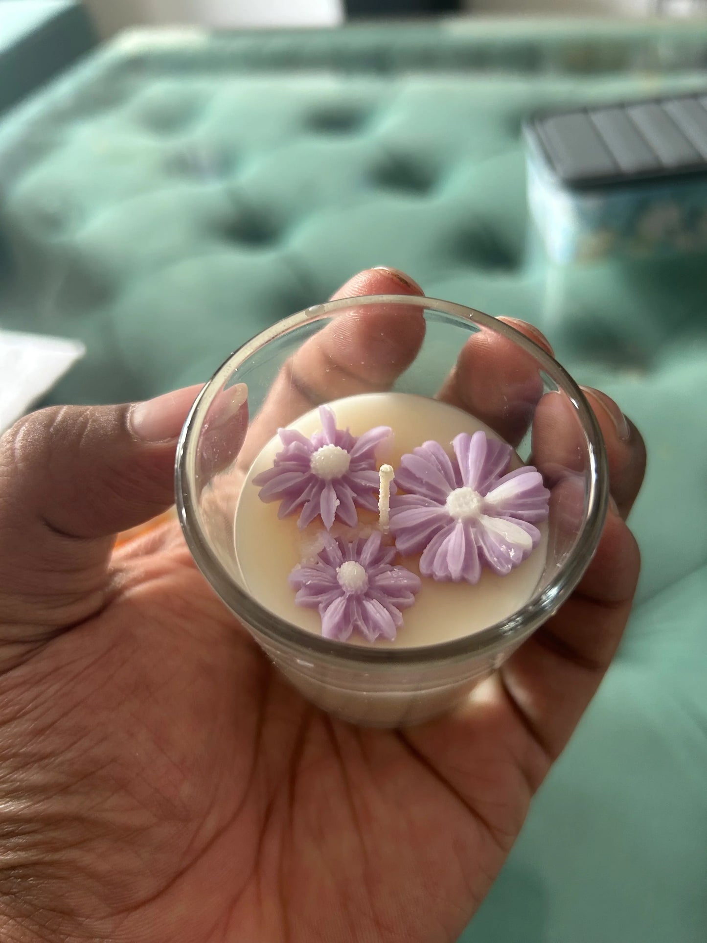 Hand holding a Fiorance Luxe soy wax candle with purple floral decorations in a glass jar