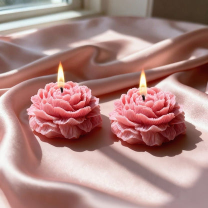 Two pink flower-shaped candles on a soft pink fabric background
