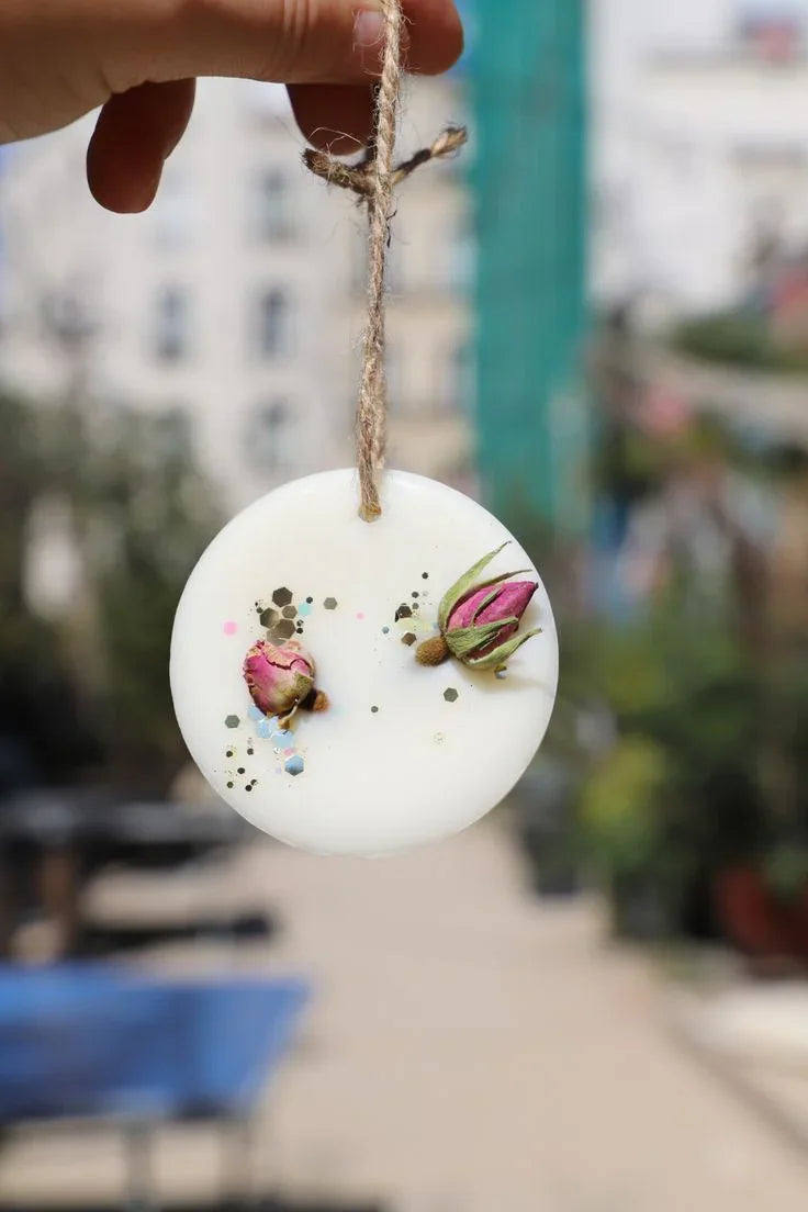 Hand holding round soy wax scented hanging ornament with dried flowers, Fiorance Luxe