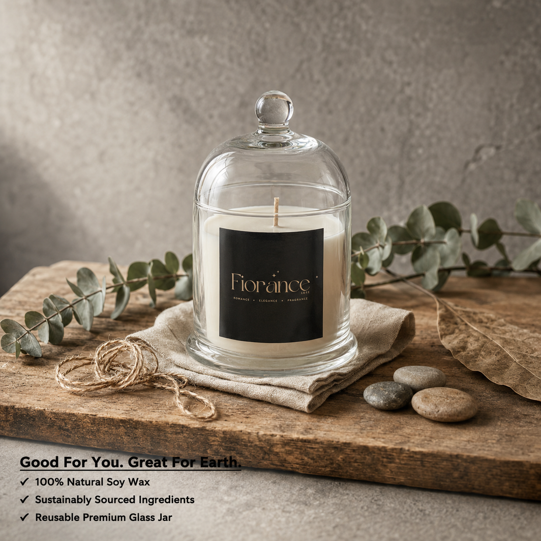 Fiorance candle in a bell glass jar on a wooden surface with eucalyptus leaves and stones.