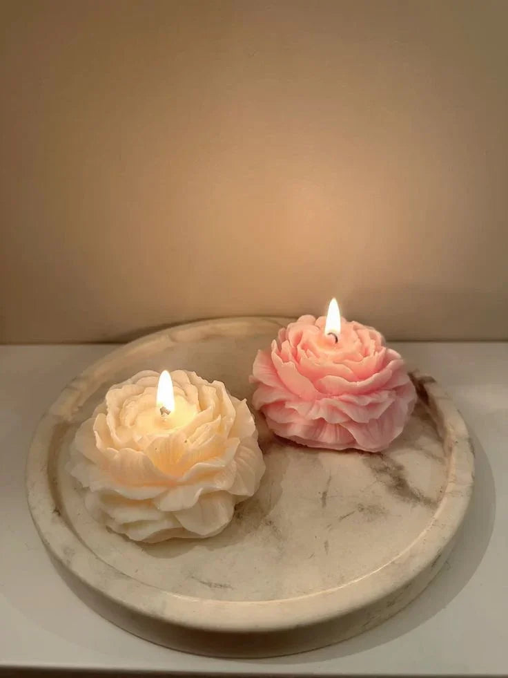 Two flower-shaped candles, one white and one pink, on a marble surface with a soft background.