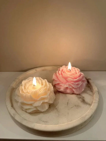 Two flower-shaped candles, one white and one pink, on a marble surface with a soft background.