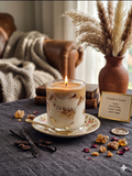 Fiorance candle on a table with vanilla beans, dried flowers, and a vase in the background.