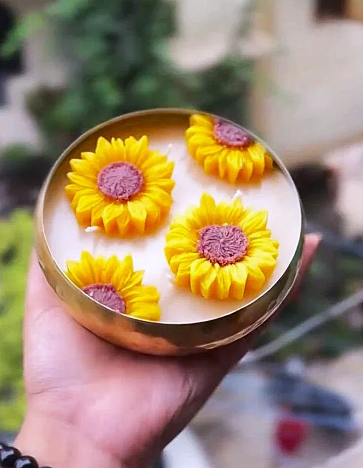 Candle with sunflower designs held by a hand against a blurred natural background