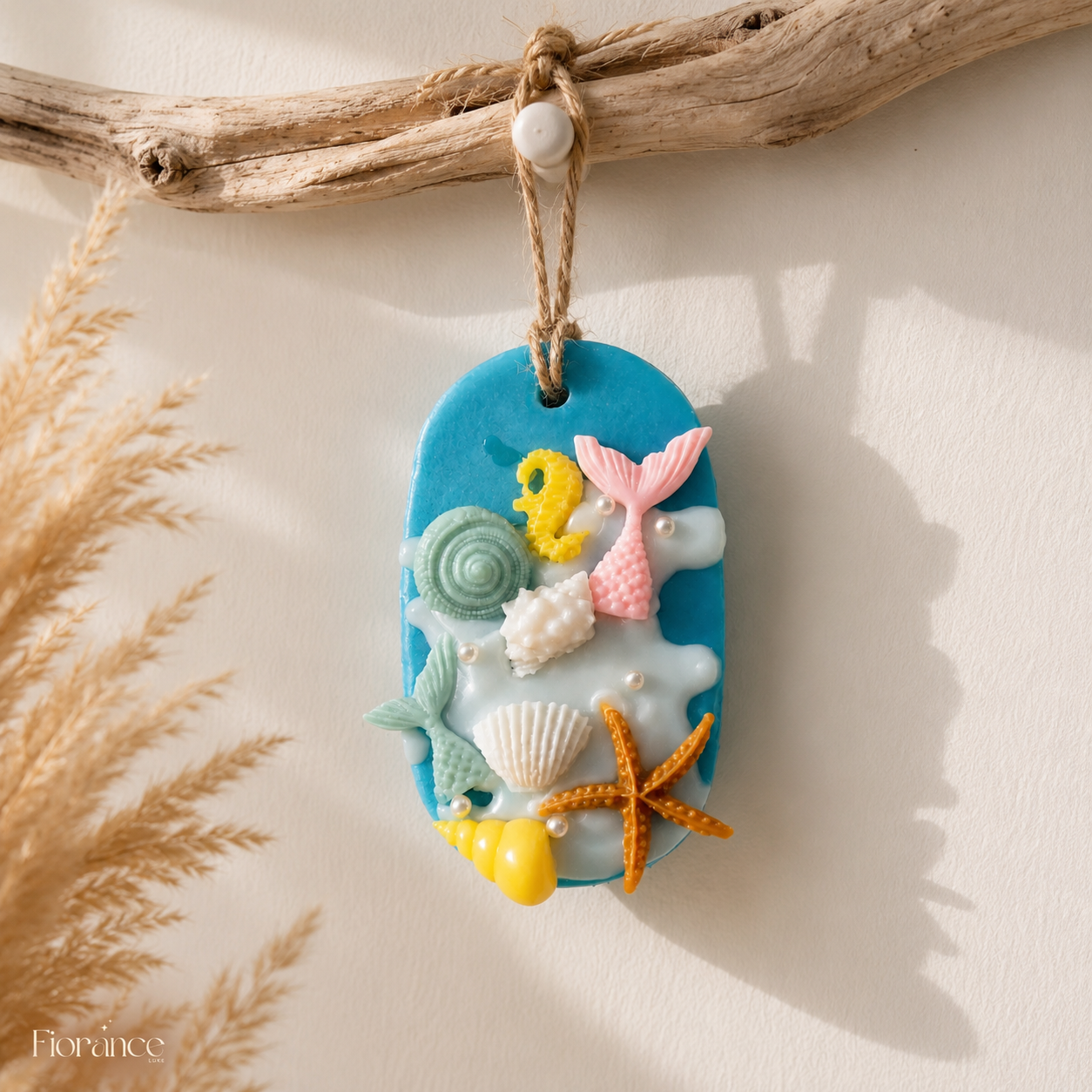 Fiorance Luxe Mermaid Ocean wax sachet hanging from natural driftwood against a cream wall with soft pampas grass shadows.