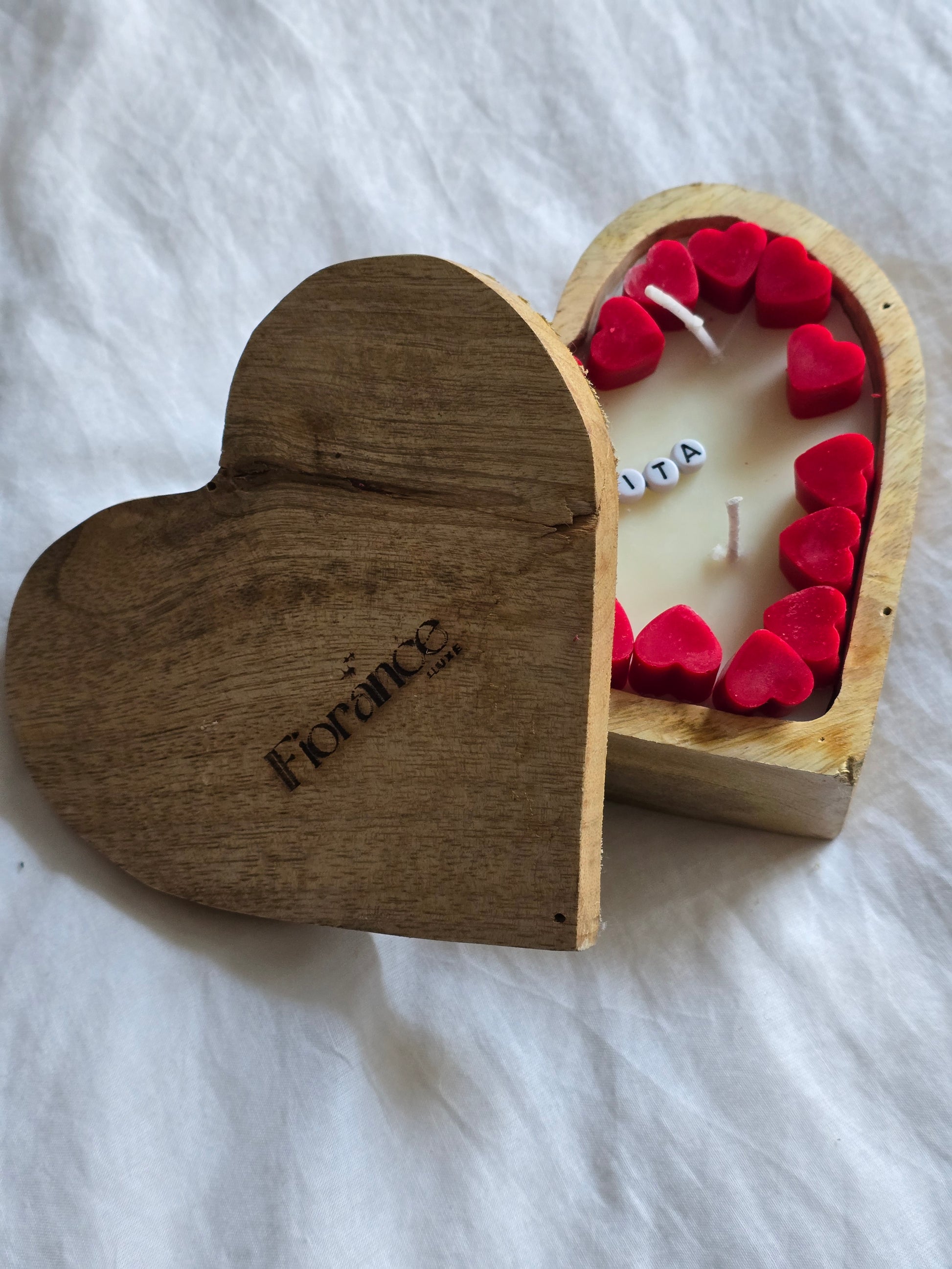 Wooden heart-shaped box with a candle and red hearts on a white fabric background