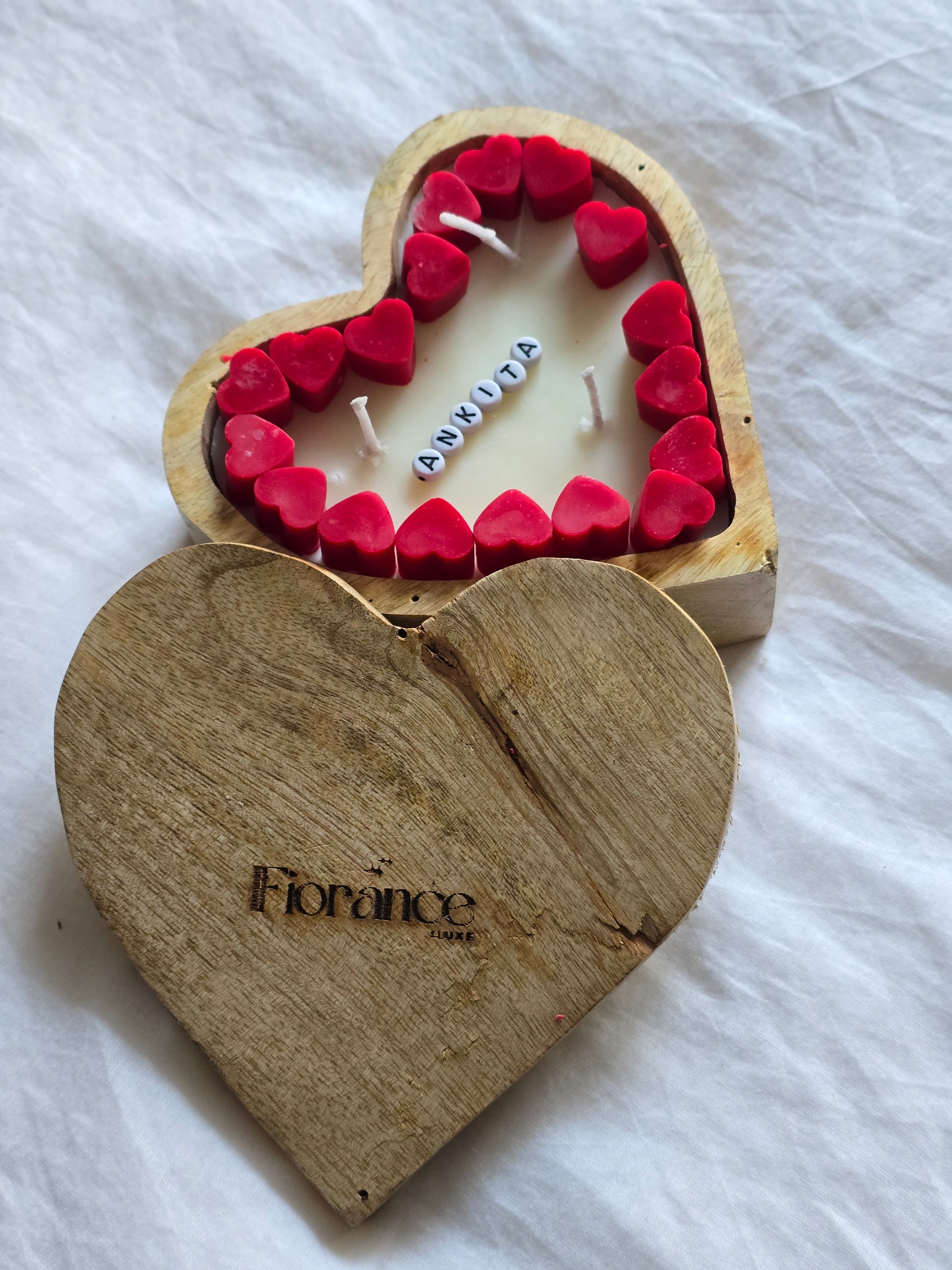 Heart-shaped wooden candle with red heart-shaped wicks on a white fabric background
