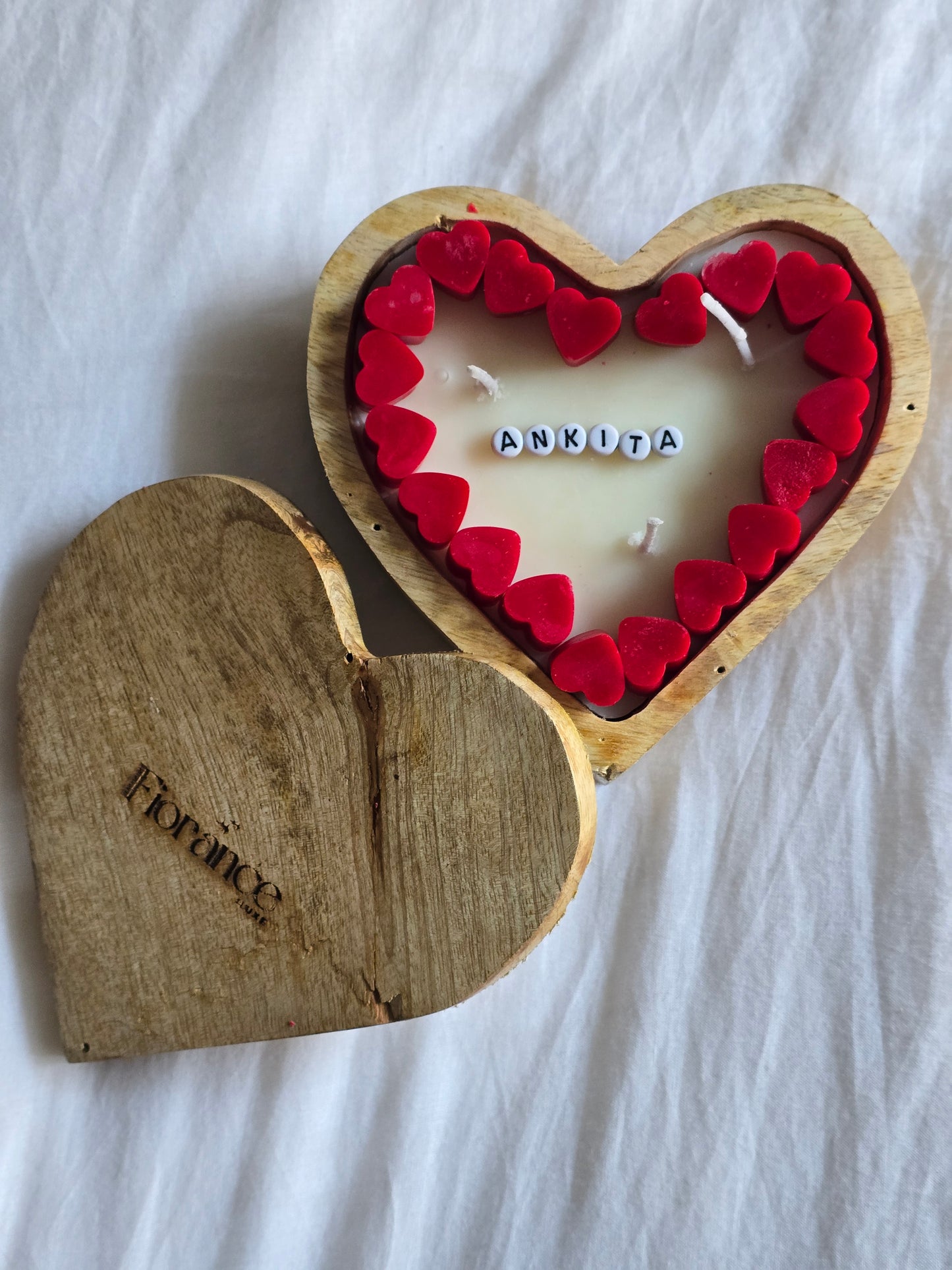 Heart-shaped candle with red wafers and wooden holder on a white fabric background