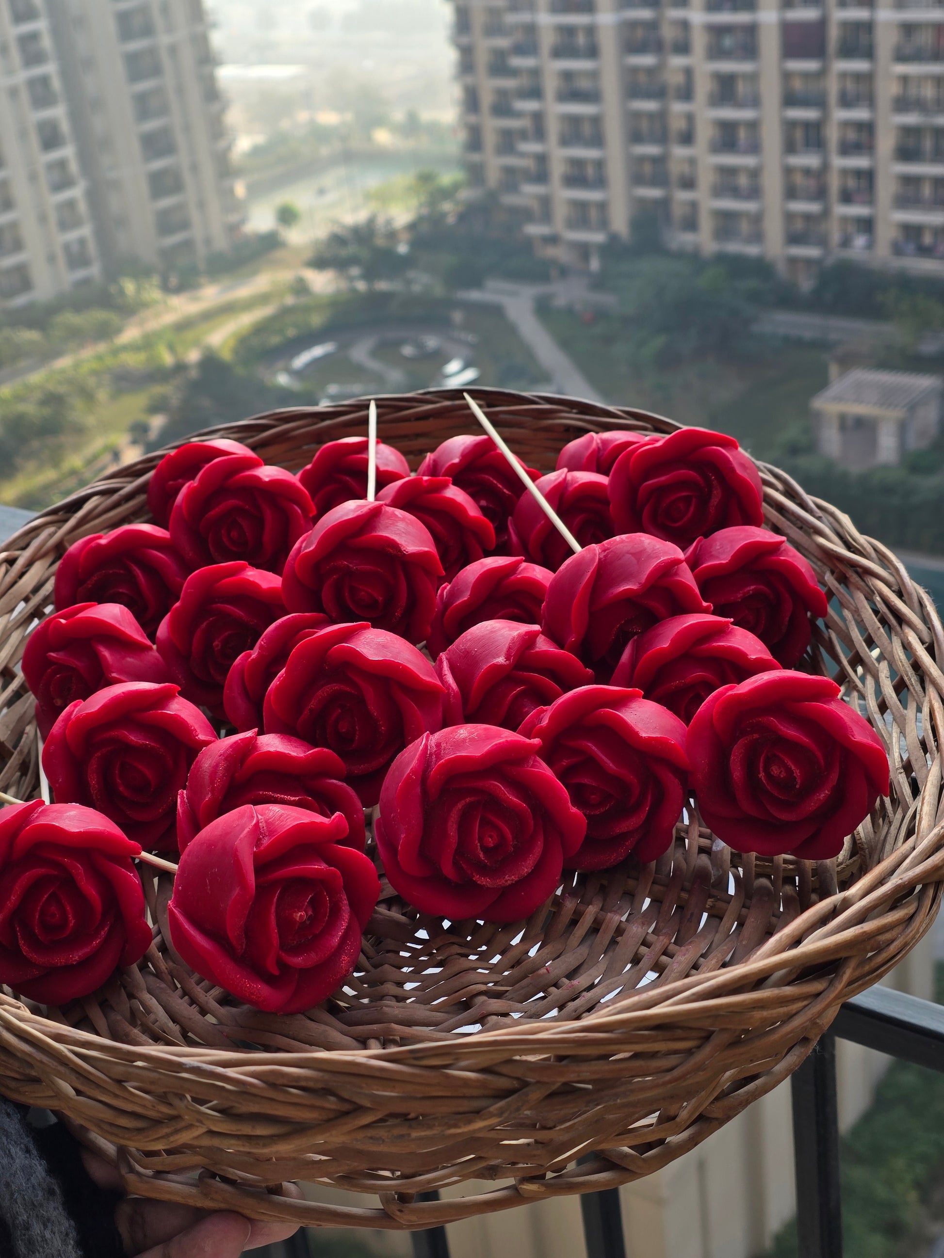 Basket of red rose-shaped Fiorance Luxe soy wax candles on balcony, cityscape background