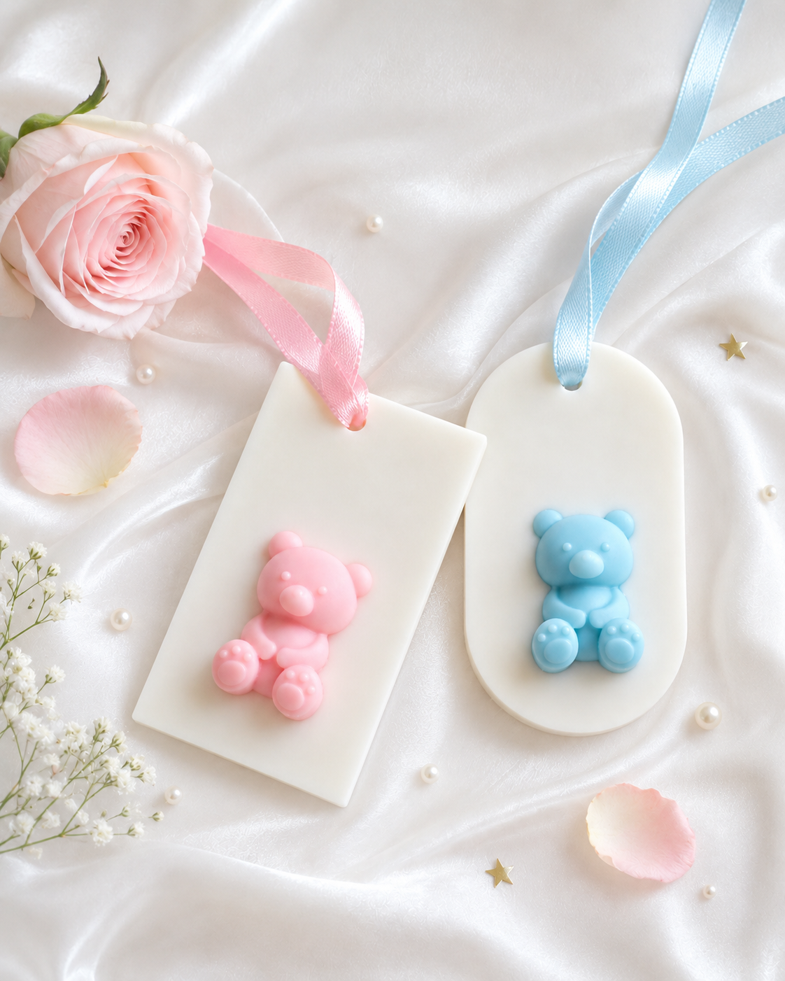 Two heart-shaped wax sachet with pink and blue bear designs on a white surface with flowers and ribbons.